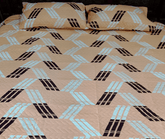 Beige bedspread with black and blue geometric pattern on a bed.
